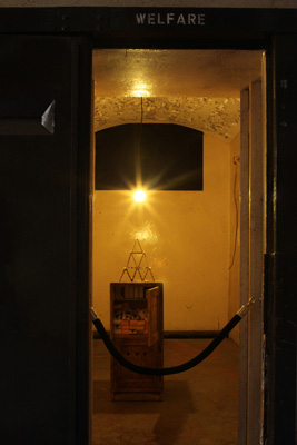 Sam McKee, Ready for a fall, bronze 30x35cm, wooden cabinet, boxes, yellow bulb, 2008 – 2009; photo Joanna Karolini